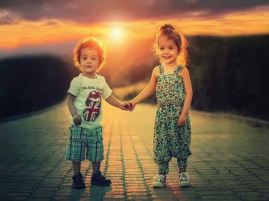 2 little kids boy and girl holding hands in the sunset
