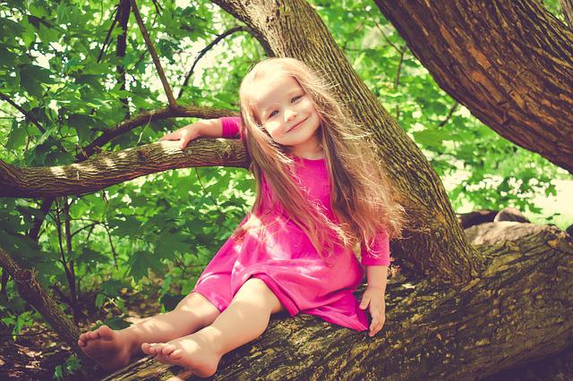 sturdy kids summer girl playing on a tree in a dress